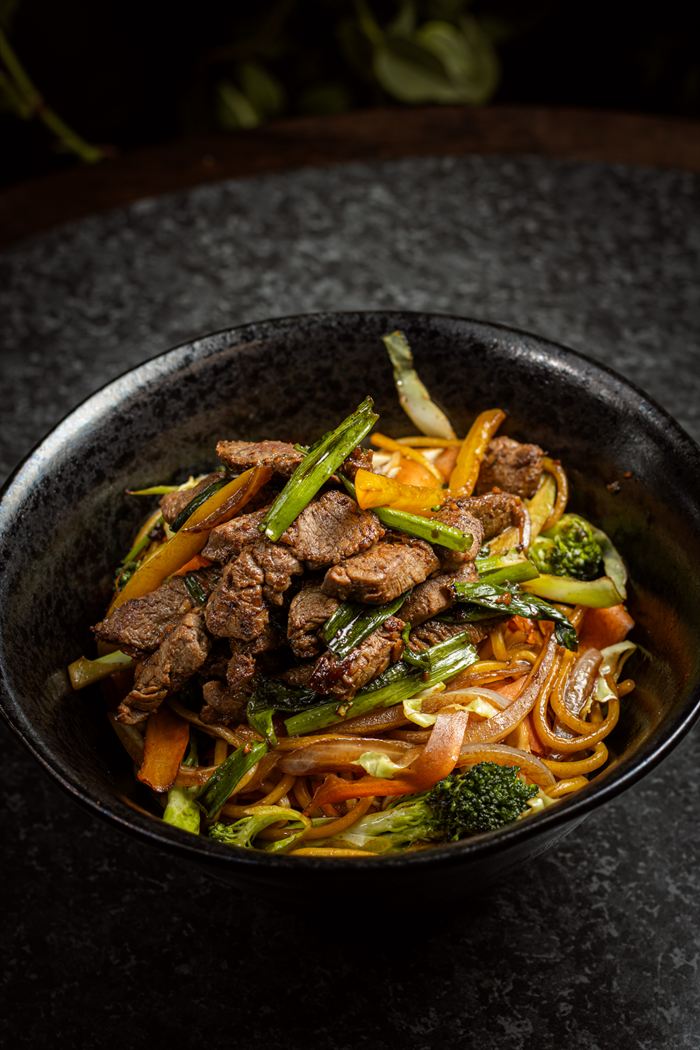Yakisoba com carne e legumes em tigela preta